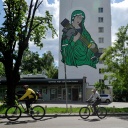 Radfahrer fahren an einem Wandgemälde vorbei, das die heilige Maria mit einer Panzerabwehrlenkwaffe in den Händen zeigt.