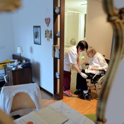 Eine Krankenschwester versorgt eine im Rollstuhl sitzende Bewohnerin in einem Pflegeheim.