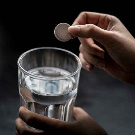 Eine Frau wirft eine Tablette gegen Eisenmangel in ein Glas Wasser. 