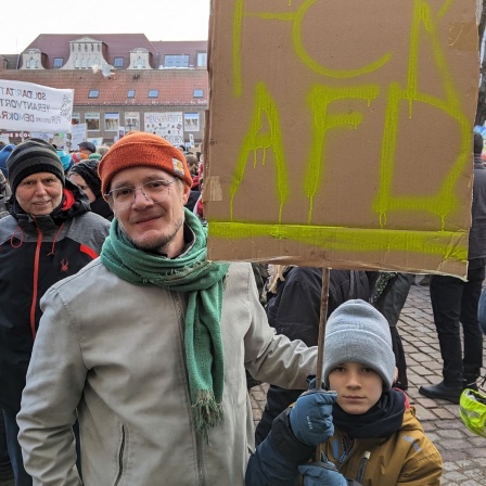 Ein Junge steht neben einem Mann und hält ein Plakat mit dem Schriftzug FCK AFD in seinen Händen bei einer Demonstration in Lübeck auf dem Rathausplatz gegen Rechtsextremismus.