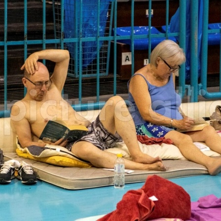 Zwei Urlauber liegen auf einer Matratze in einer Turnhalle.