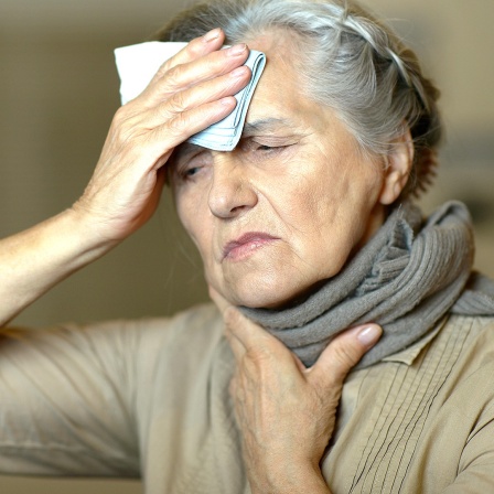 Frau mit Hals- und Kopfschmerzen hält sich ein Taschentuch an die Stirn. 