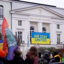 Demonstration gegen den Krieg Russlands in der Ukraine vor dem Deutschen Theater, an dem ein Banner in ukrainischen Farben mit dem Schriftzug "Stay united" hängt.