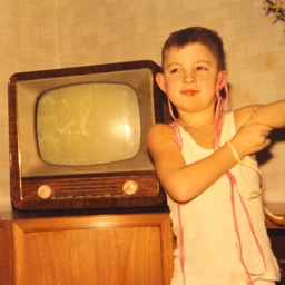 Ein Junge steht im Wohnzimmer vor dem Fernseher. Er hat Luftschlangen an den Ohren hängen.