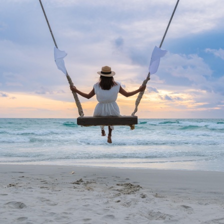 Eine Frau auf einer Seilschaukel am Strand beobachtet den Sonnenuntergang