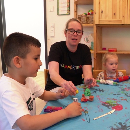 Kita-Chefin Nancy Wullf sitzt mit Kindern am Tisch.