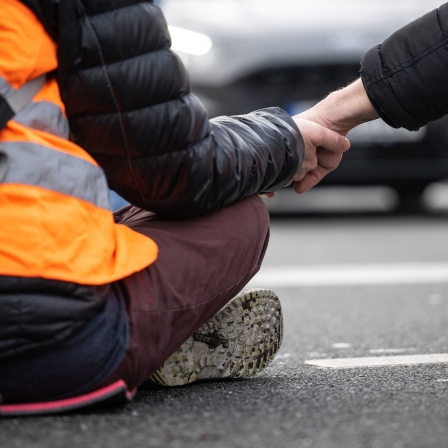 Klimaaktivisten der Gruppe "Letzte Generation" haben ihre Hände zusammengeklebt, um eine Straße  zu blockieren.
