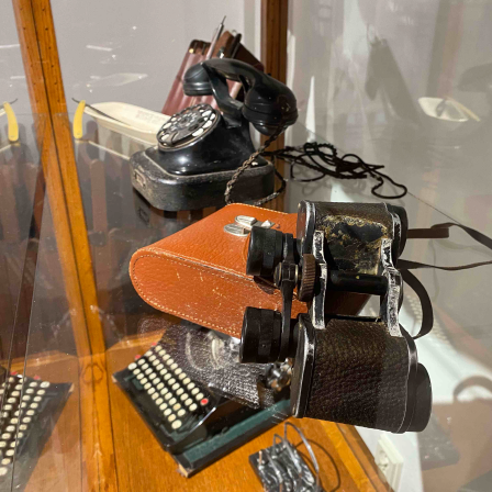 In einer Vitrine stehen ein altes Fernglas sowie ein Telefon mit Wählscheibe