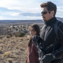Eine Szene des Films Sicario: Ein bewaffneter Mann steht mit einer jungen Frau im Grenzland zwischen den USA und Mexico. Im Hintergrund ist karge Natur zu sehen