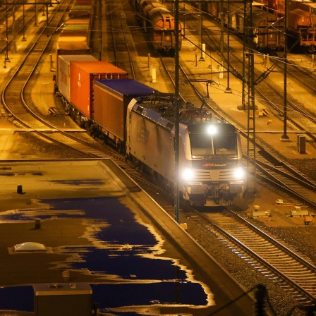 Güterzug fährt nachts in beleuchtetem Bahnhof.
