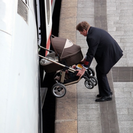 Ein Mann hieft einen Kinderwagen in einen ICE.