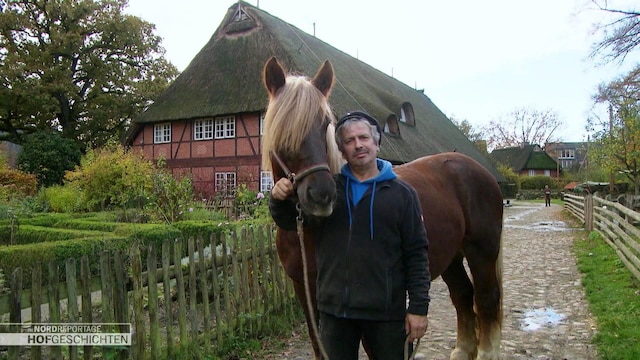 Ein Mann steht mit einem Pferd vor einem Haus.