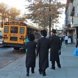 Drei in schwarz gekleidete Männer gehen in den USA auf einem Bürgersteig, daneben ist ein gelber Bus