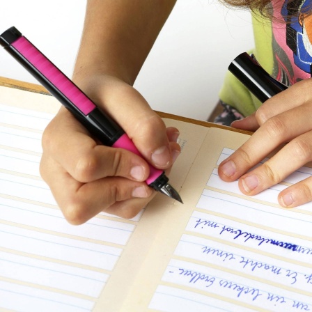 Schulmädchen schreibt mit einem Füller in ein Heft