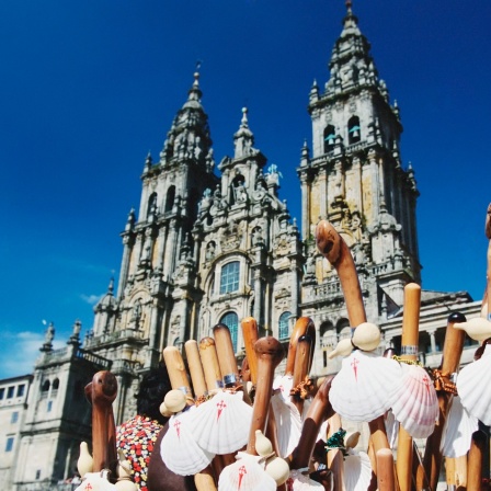 Türme der Kathedrale von Santiago de Compostela hinter einem Verkaufsstand mit Symbolen des Jakobswegs, Jakobsmuscheln