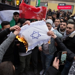 Männer verbrennen 2017 in Berlin Neukölln eine selbst gemalte Israel-Fahne. Im Hintergund ist die türkische und die palästinensische Flagge zu sehen. Einige tragen Kefia.