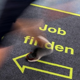 Ein Mann geht in einem Jobcenter über einen Teppich mit der Aufschrift "Job finden". (Gestellte Szene)