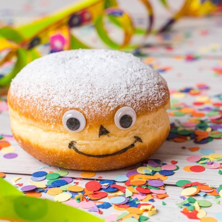 Leckerer Berliner mit niedlichem Gesicht in Faschingsdeko: Feuchter Zucker klebt, weil Zucker und Wasser etwas gemeinsam haben, das sie buchstäblich verbindet: Wasserstoff
