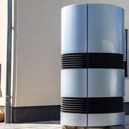Eine Luft- und Wasserwärmepumpe steht vor dem Eingang eines Wohnhauses.