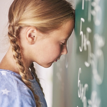 Ein Mädchen lehnt ihren Kopf an eine Tafel. Ihre Augen sind geschlossen.