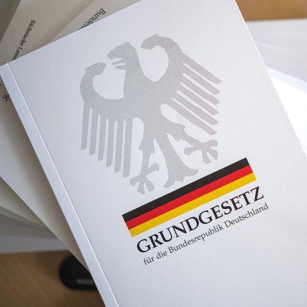Eine Ausgabe des Grundgesetzes der Bundesrepublik Deutschland liegt neben Schreibutensilien.