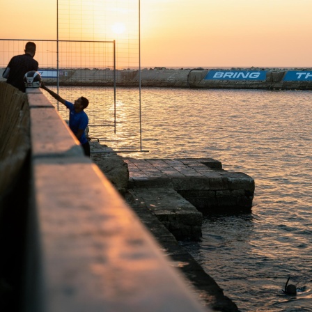 Zwei Fischer und ein Taucher im Hafen von Jaffa am 1. November 2023. Auf der gegenüberliegenden Seite lässt sich auf einer Mauer in großen Lettern "Bring them home" - "Bringt sie heim" lesen.
