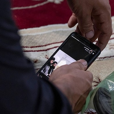 Ein Mann hält ein Smartphone in der Hand; es sind lediglich seine beiden Hände zu sehen. Auf dem Bildschirm des Handys sind Angehörige der Taliban zu sehen (21.08.2021)