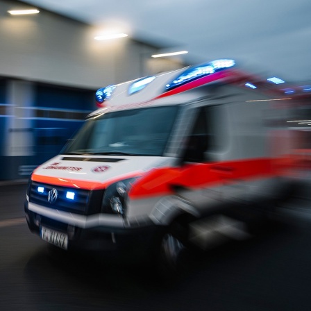 Ein mit Bewegungsunschärfe fotografierter Rettungswagen fährt mit Blaulicht über eine Straße.