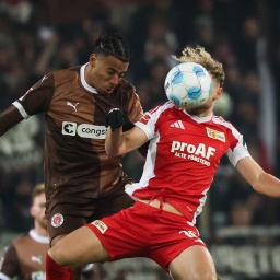 Die beiden springen zum Kopfball hoch. Guliavogui trägt ein braunes Trikot; Hollerbach ein weiß-rotes. Sein Kopf ist vom Ball verdeckt. 