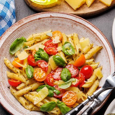 Teller mit Pasta und Tomaten sowie Basilikum, mit gebratenen Garnelen und grünem Spargel