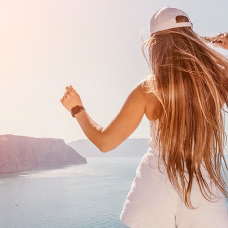 Eine Frau von hinten, die aufs Meer blickt und ihre Hände hochhält, als würde sie vor Freude tanzen.