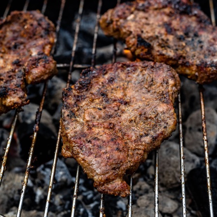 Auf dem Grill liegen drei Fleischstücke.