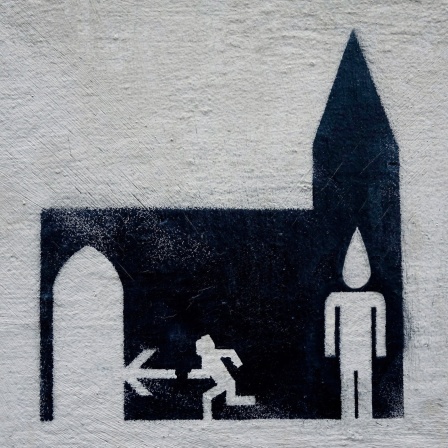 Ein Graffiti an einer Bonner Hauswand zeigt ein Piktogramm-Männchen, das aus einer Kirche rennt