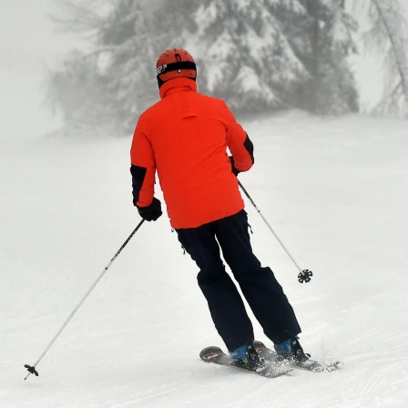 Skifahrer auf einer verschneiten Piste im Nebel. Symbolbild