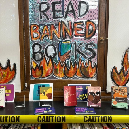 Hinter einem Büchertisch ist ein Fenster mit der denalten Aufschrift: Read banned books
