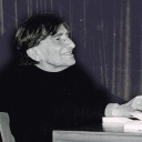Eine ältere Frau mit kurzen, dunklen Haaren sitzt an einem Tisch, ihre Hände liegen auf einem aufgeschlagenen Buch, Charlotte Wolff, vermutlich 1978 in Berlin fotografiert