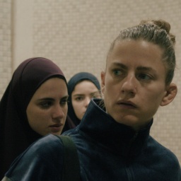 Szene aus dem Film "Mond": Eine junge blonde Frau im Vordergrund, im Hintergrund zwei junge Frauen mit Kopftuch