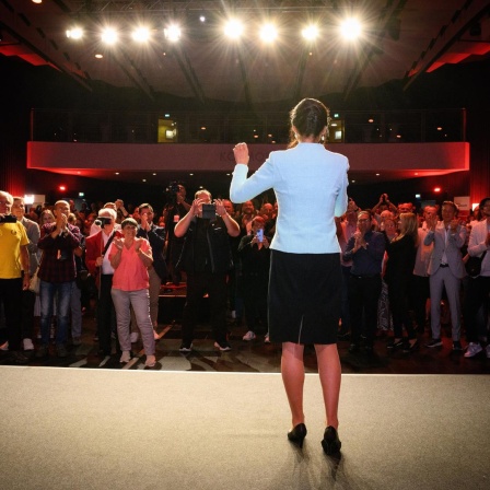 Sahra Wagenknecht steht auf einer Bühne. Vor ihr Menschen, die zujubeln. Darüber Scheinwerfer, die Wagenknecht ins Rampenlicht rücken.