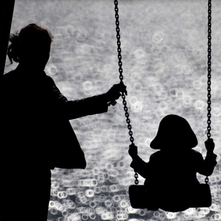  Eine Mutter schaukelt ihr Kind auf einem kleinen Spielplatz am glitzernden Wasser der Alster.