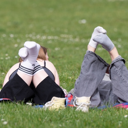 Auf einer Wiese liegen zwei Menschen nebeneinander auf dem Bauch und haben die Beine angewinkelt.