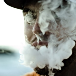 Das Gesicht eines jungen Mannes ist durch den Rauch seiner E-Zigarette verhüllt. 