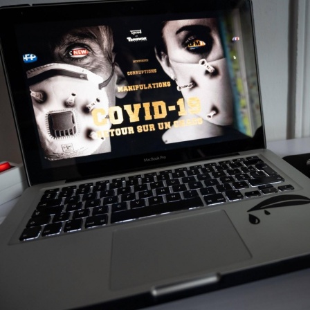Ein Laptop hat den Streaming-Film "Hold Up" des früheren französischen Journalisten Pierre Barnérias geladen, der angeblich die Wahrheit über Covid-19 erzählt. Auf dem Bildschirm sieht man recht und links je ein Gesicht mit Maske und in der Mitte ste
