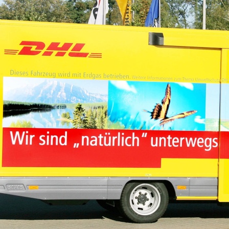 Mitarbeiter von DHL stehen an einer Erdgastankstelle in Leipzig neben einem neuen DHL-Fahrzeug, das mit Erdgas fährt.