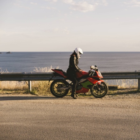 Eine Motoradfahrerin auf ihrem Motorrad an einer Küste.
