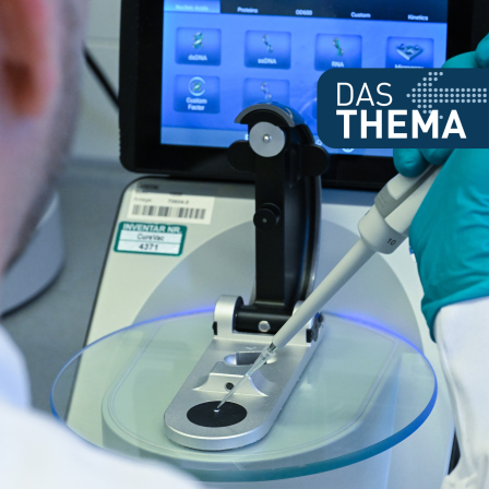 eine Nahaufnahme eines Laborexperiments. Eine Person in einem weißen Laborkittel und blauen Schutzhandschuhen verwendet eine Mikropipette, um eine Flüssigkeit auf eine Analyseplatte oder ein Testgerät aufzutragen. Im Hintergrund befindet sich ein Bildschirm mit einer wissenschaftlichen Benutzeroberfläche, auf der Begriffe wie „RNA“ und „Microarray“ zu sehen sind. Dies deutet darauf hin, dass es sich um eine biotechnologische oder genetische Analyse handelt, möglicherweise im Zusammenhang mit der Krebsforschung oder molekularbiologischen Untersuchungen. In der oberen rechten Ecke befindet sich ein Schriftzug „DAS THEMA“