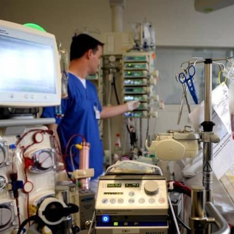 In einem Zimmer auf der Intensivstation bedient ein Mediziner eine Maschine zur Versorgung eines Patienten