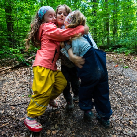 Drei Kinder stehen auf einem Waldweg und umarmen sich.