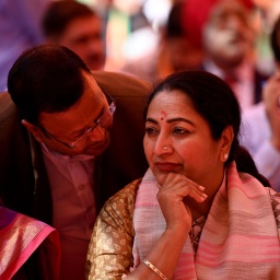 Delhis Ministerpräsidentin Rekha Gupta sitzt das Kinn auf die Hand gestützt in traditionell indischer Kleidung in einer Gruppe von Männern. Jagat Prakash Nadda, Vorsitzender der BJP-Partei, lehnt über ihrer Schulter und spricht ihr ins Ohr.
