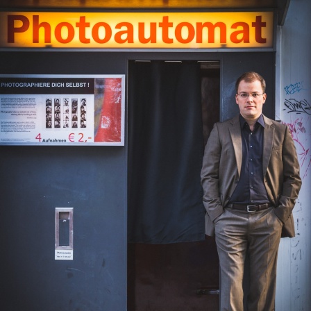 Philipp Ahmann, Künstlerischer Leiter des MDR-Rundfunkchors, lehnt an einem Fotoautomaten