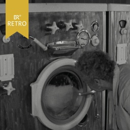 Eine ältere Frau schaut in das Fenster einer laufenden Waschmaschine | Bild: BR Archiv